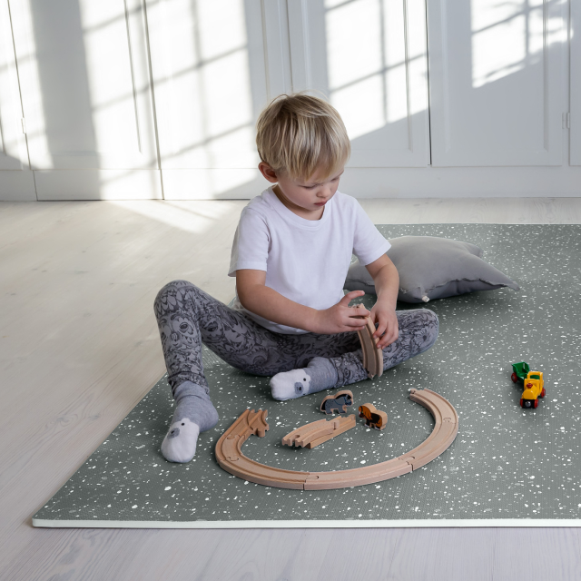 Child playing with toy train tracks on a mat