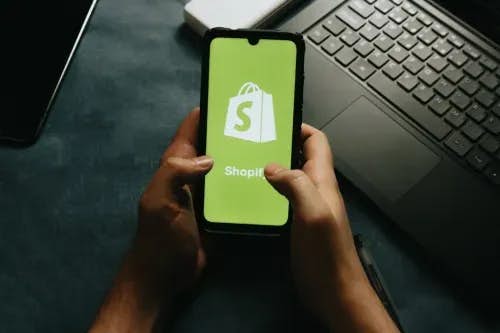 Hands hold a cell phone showing the Shopify logo